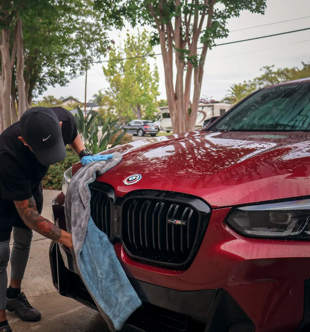 Technician drying a red BMW with a microfiber towel after a hand wash